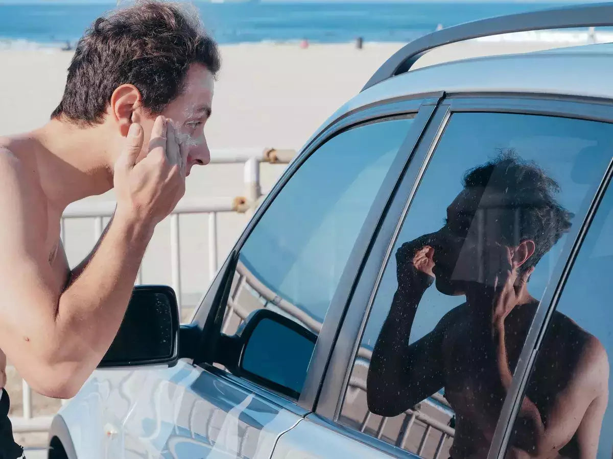 man applying sunscreen to face looking in car window reflection